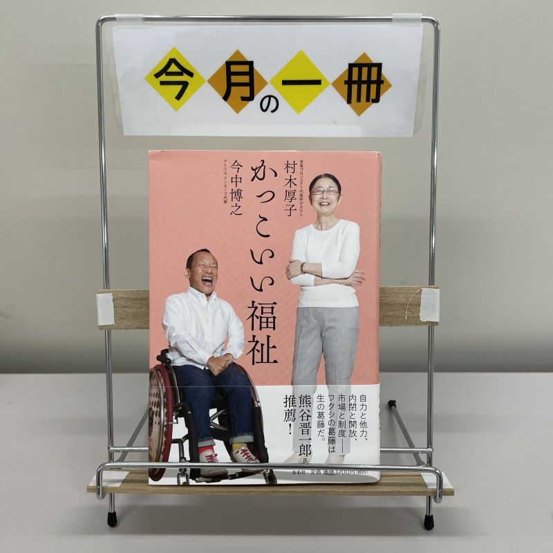 本の表紙の画像。車いすの男性１人、立っている女性１人が笑っている。